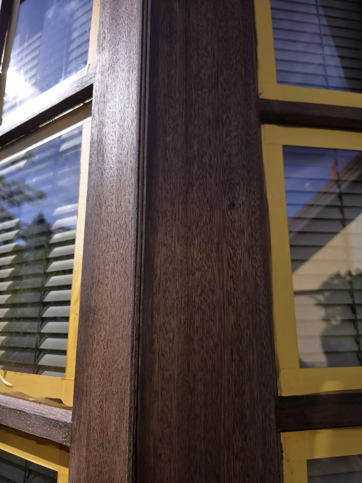 Holzfenster lasiert: Eckpfosten mit neuer dunkelbrauner Lasur, die Holzmaserung bleibt sichtbar, das Glas ist noch abgeklebt