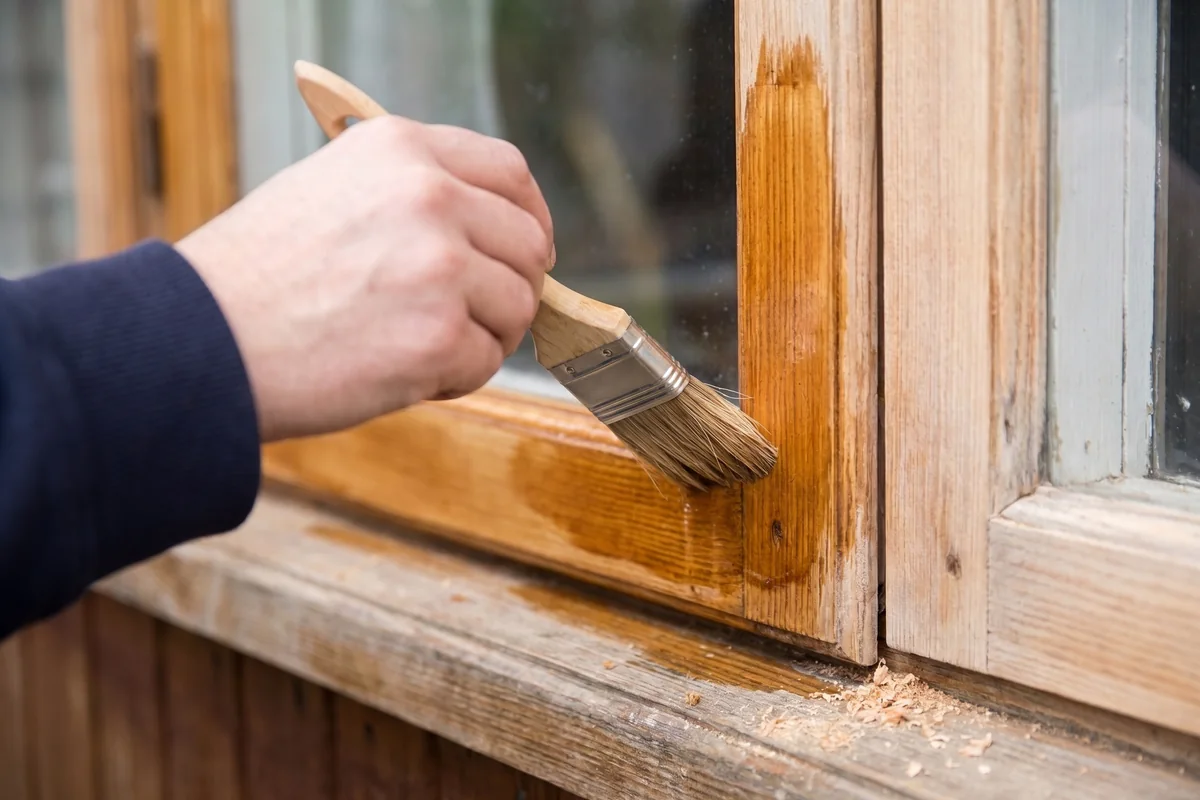 Holzfenster lasieren: Pinsel trägt eine warme Eichen-Lasur auf den geschliffenen Fensterrahmen auf, die Holzmaserung bleibt sichtbar